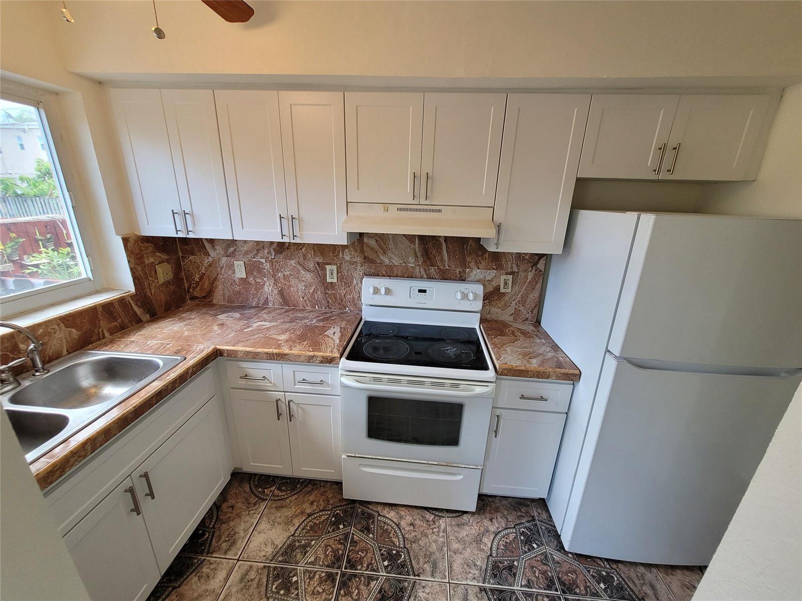 A kitchen features white cabinets, brown marble-patterned countertops, a white stove, and patterned floor tiles — 8451 NW 4th Avenue # 8451, Miami FL 33150, MIAMI, FL