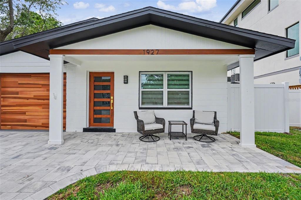 A modern house exterior features a white facade, wood-paneled garage door, and a paved porch — 1927 SHORE ACRES BOULEVARD NE, ST PETERSBURG, FL