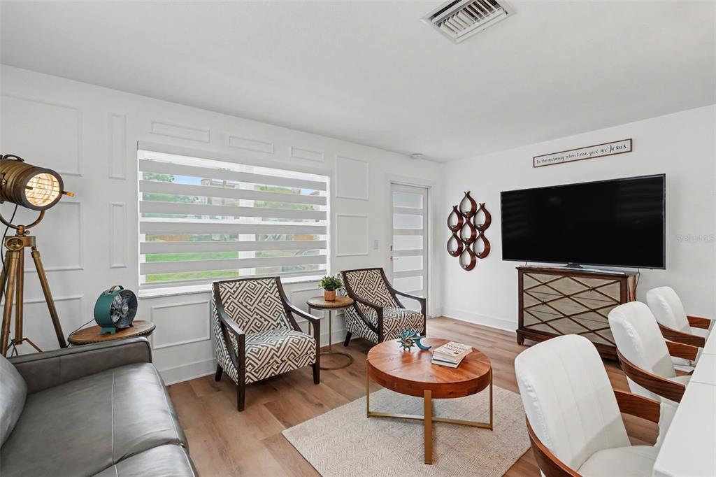 A living room features white paneled walls, wood flooring, patterned armchairs, and a large television — 1927 SHORE ACRES BOULEVARD NE, ST PETERSBURG, FL