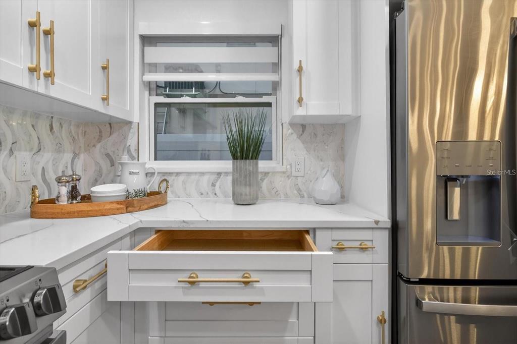 A kitchen features white cabinets, gold hardware, a marble-patterned backsplash, and a stainless steel refrigerator — 1927 SHORE ACRES BOULEVARD NE, ST PETERSBURG, FL