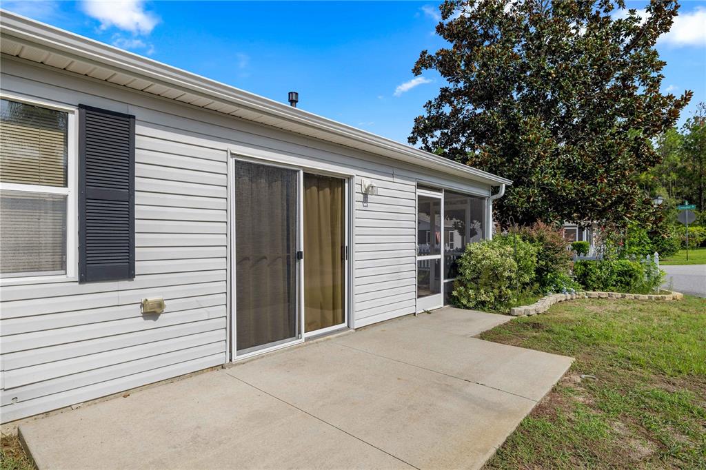 A light gray vinyl-sided house features a concrete patio, sliding glass doors, and a screened porch — 272 EMMALEE PLACE, THE VILLAGES, FL
