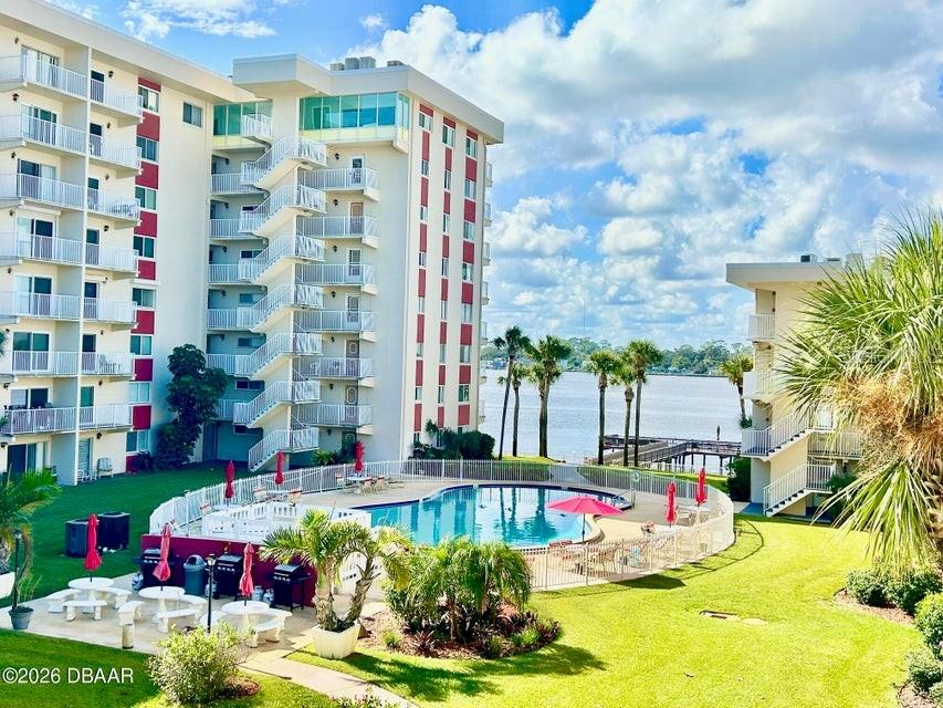 An outdoor swimming pool sits between two multi-story apartment buildings overlooking a body of water — 2711 N HALIFAX AVENUE UNIT 374, DAYTONA BEACH, FL