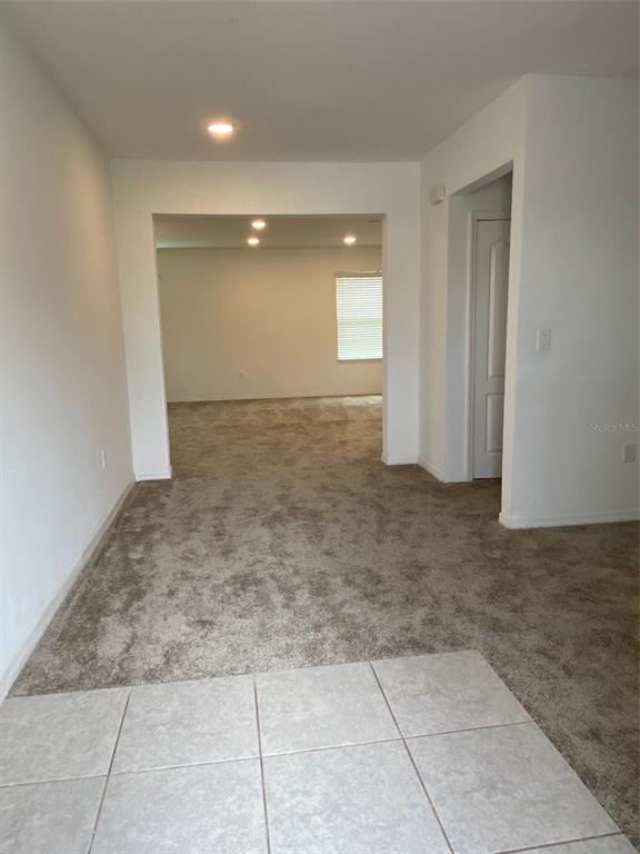 A view from a tiled area into a carpeted living room with a window — 999 CUMBERLAND DRIVE, POINCIANA, FL