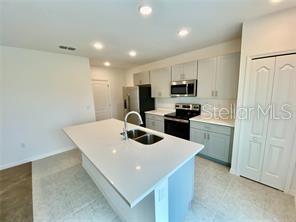 A modern kitchen features a white quartz island, light gray cabinetry, and stainless steel appliances — 999 CUMBERLAND DRIVE, POINCIANA, FL