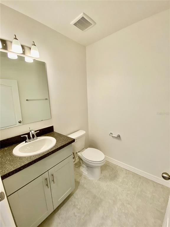 A bathroom features a vanity with a dark countertop, a toilet, and a wall mirror — 999 CUMBERLAND DRIVE, POINCIANA, FL