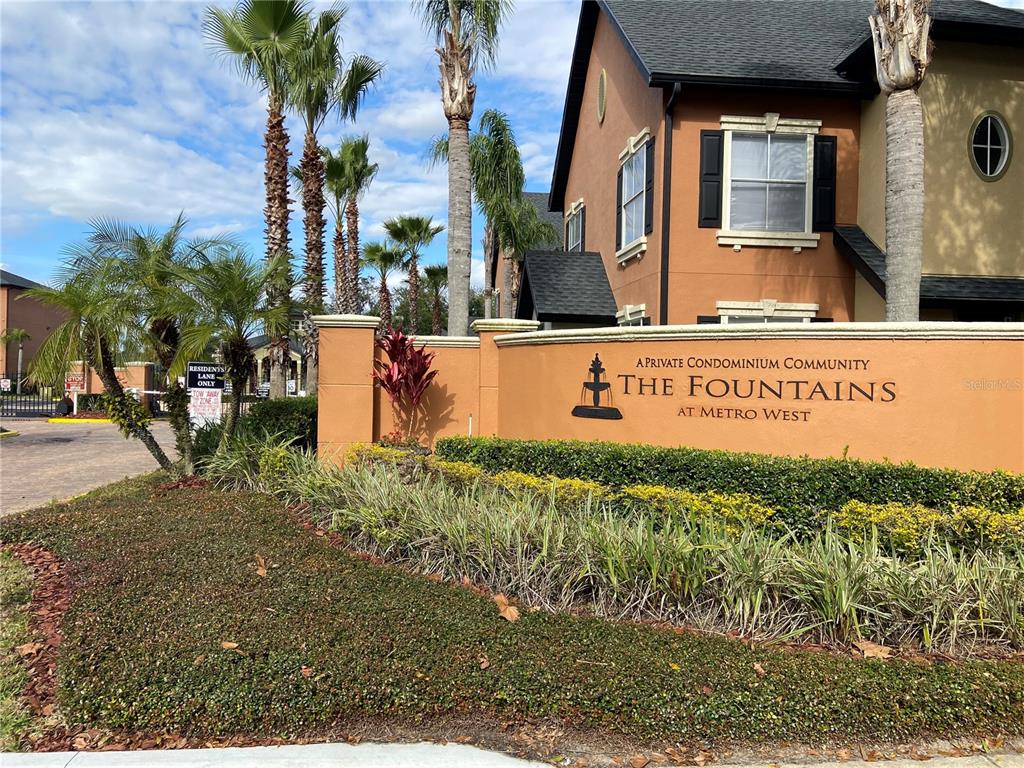 A tan stucco monument sign for The Fountains at Metro West stands before a building — 6025 WESTGATE DRIVE UNIT 2512, ORLANDO, FL