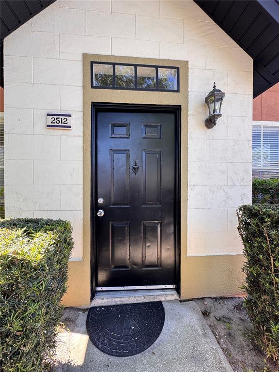 A black front door with a transom window is set into a light-colored block wall — 6025 WESTGATE DRIVE UNIT 2512, ORLANDO, FL