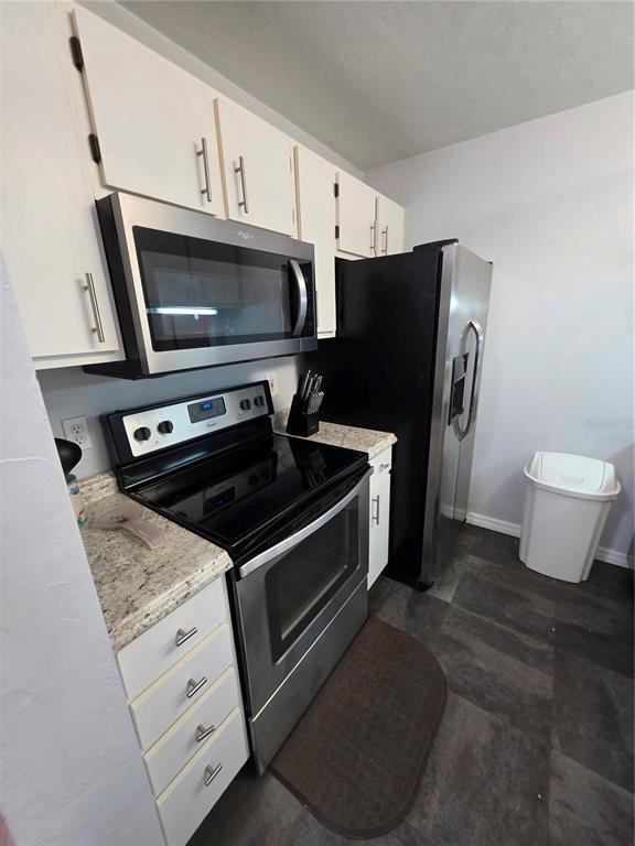 A kitchen features white cabinets, stainless steel appliances, granite countertops, and dark tile flooring — 4000 SW 23RD STREET UNIT 6-305, GAINESVILLE, FL
