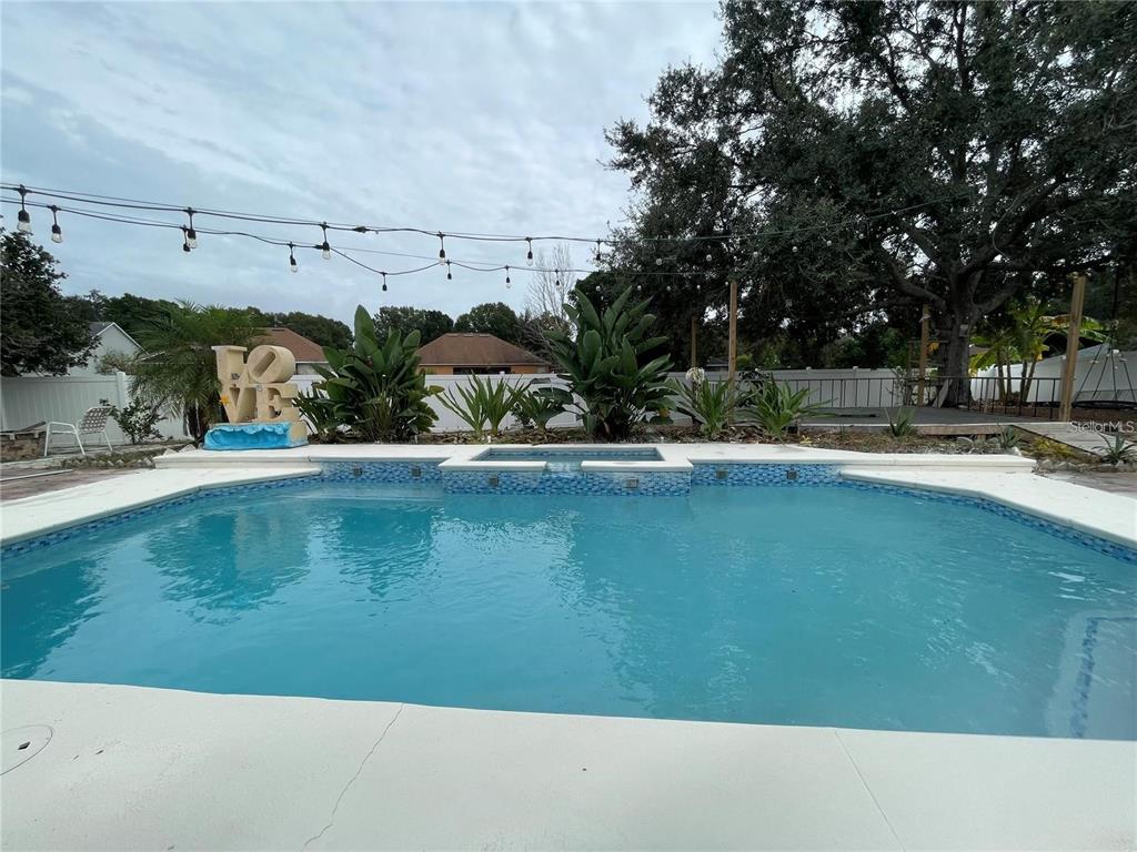 A backyard swimming pool with a spa, string lights, and landscaping under a cloudy sky — 1924 RACHELS RIDGE LOOP, OCOEE, FL