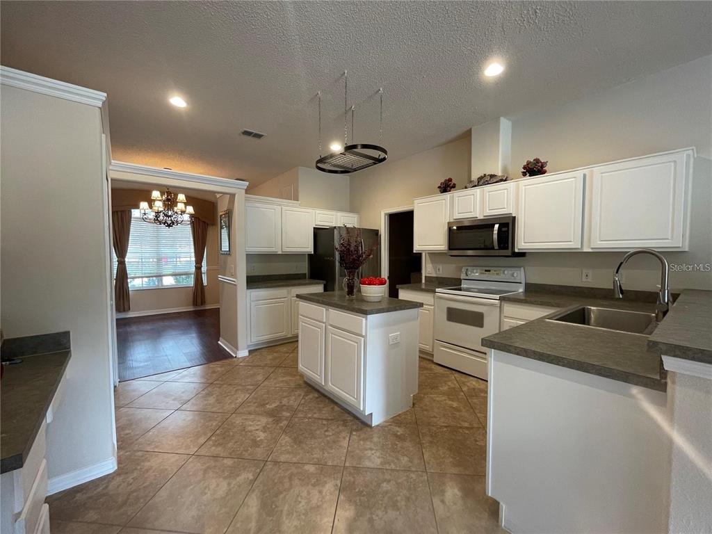 A kitchen with white cabinets, a central island, and tile flooring, adjacent to a dining area — 1924 RACHELS RIDGE LOOP, OCOEE, FL
