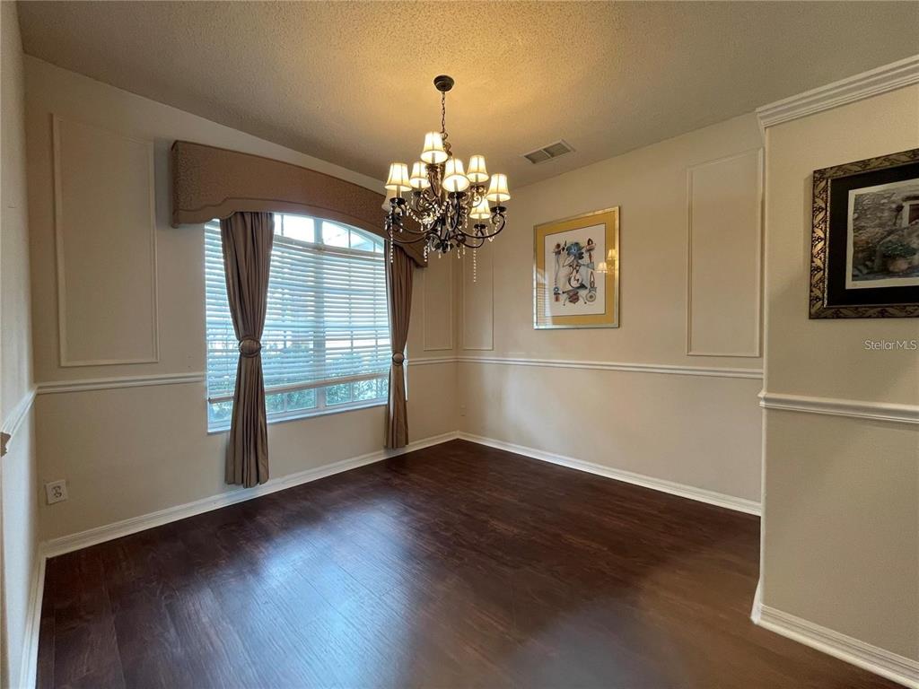 A dining room features dark wood flooring, a chandelier, and a window with curtains — 1924 RACHELS RIDGE LOOP, OCOEE, FL