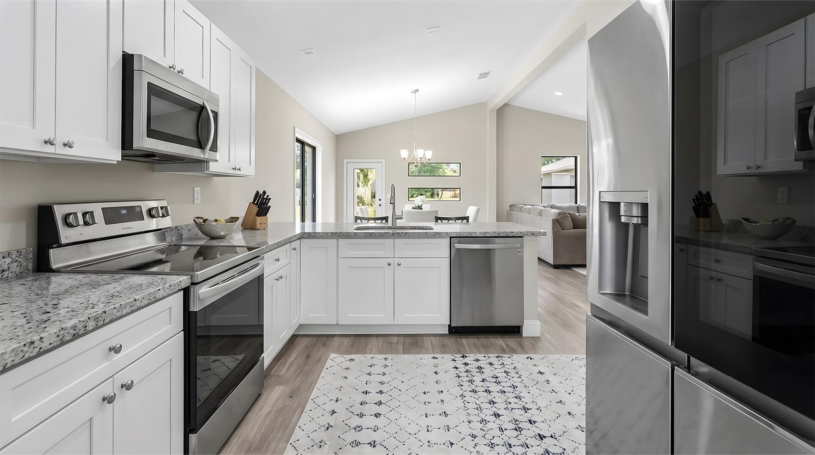 A modern kitchen with white cabinets, granite countertops, stainless steel appliances, and wood-look flooring — 8019 NW 8th Avenue, Miami FL 33150, MIAMI, FL