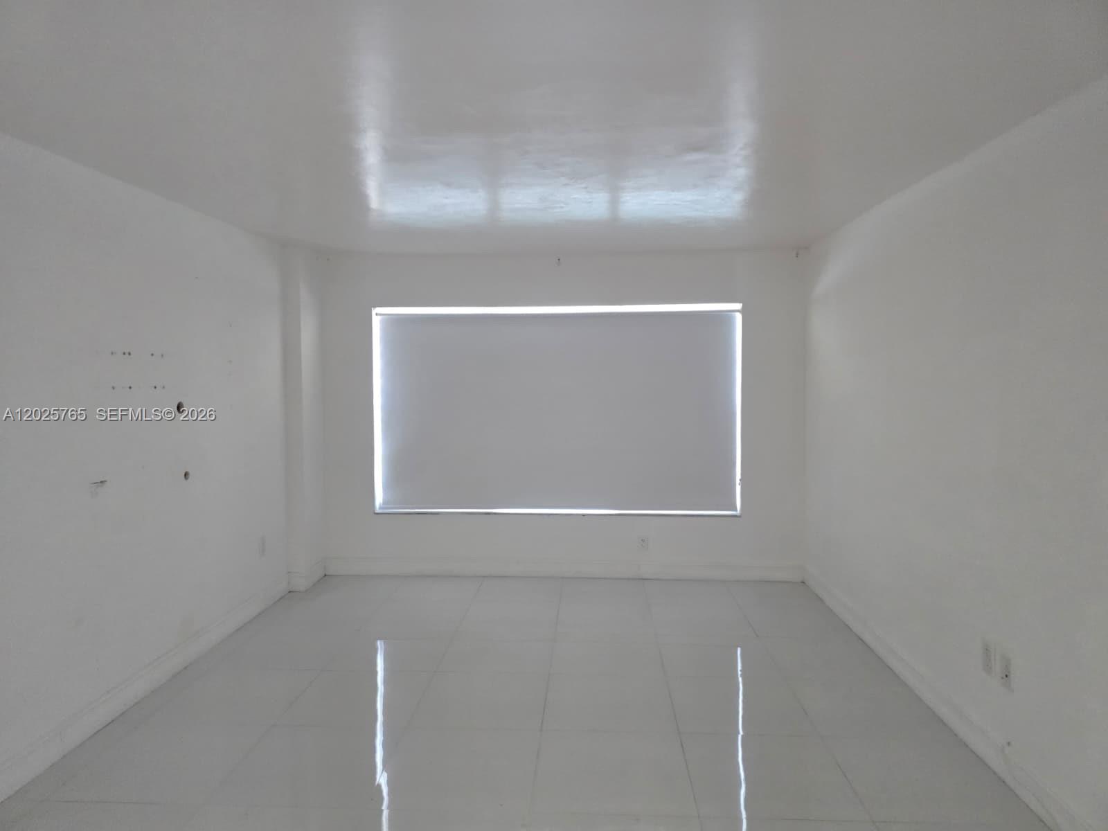 An empty room features white walls, glossy tile flooring, and a single window with a shade — 11111 Biscayne Blvd # 17D, Miami FL 33181, MIAMI, FL