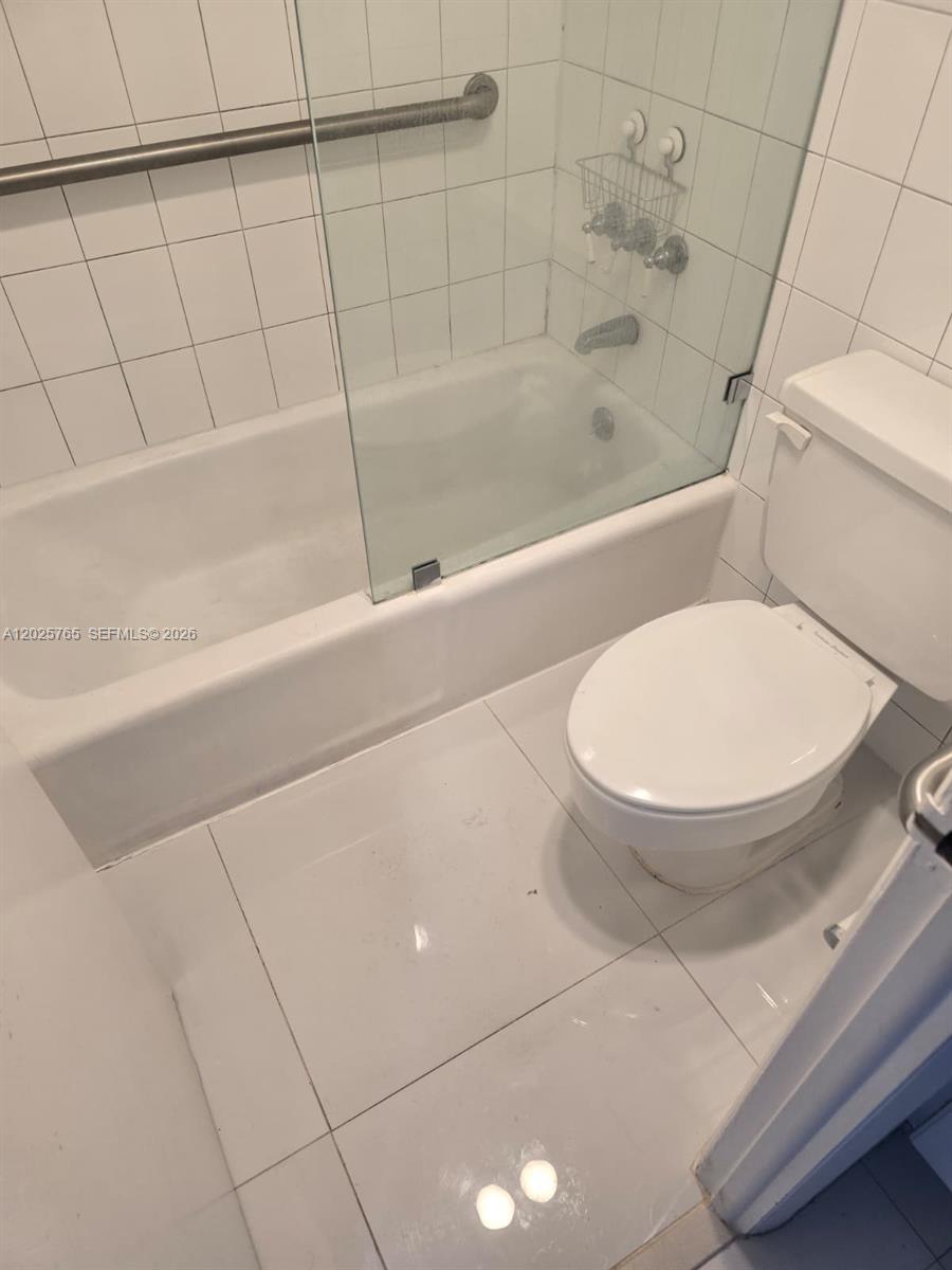 A bathroom features a white toilet, a tiled bathtub with a glass screen, and grab bars — 11111 Biscayne Blvd # 17D, Miami FL 33181, MIAMI, FL