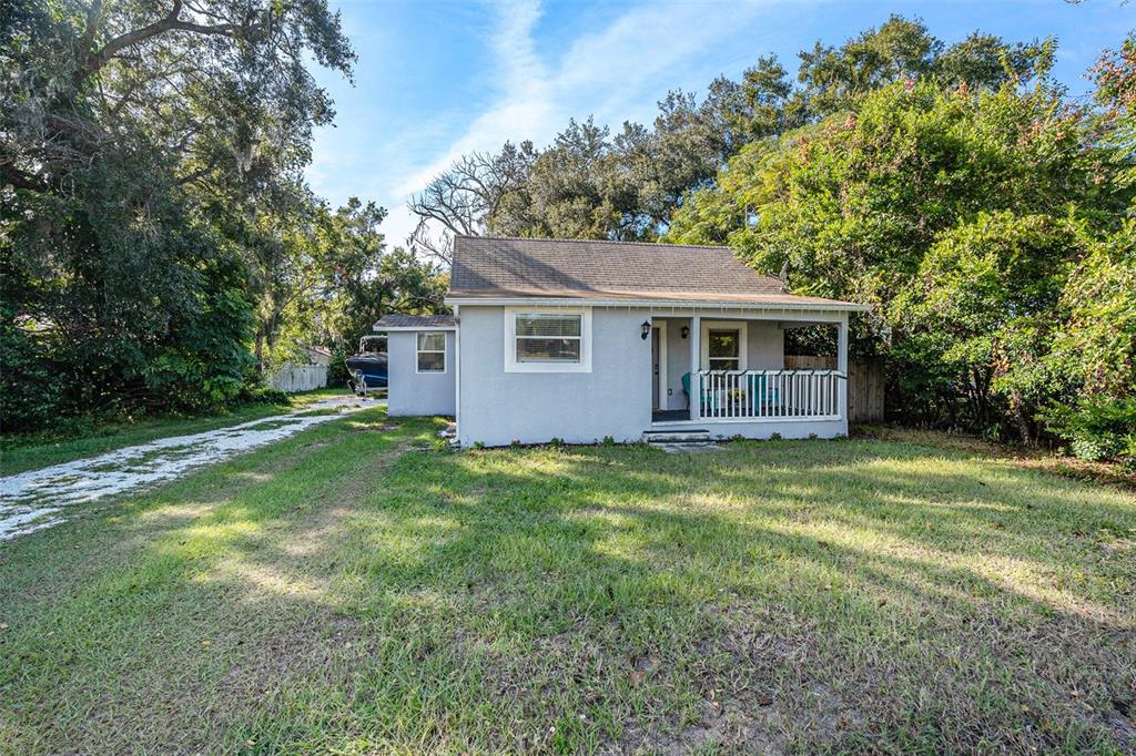 A small, light-gray house with a covered front porch sits on a grassy lot — 4921 6TH STREET, ZEPHYRHILLS, FL
