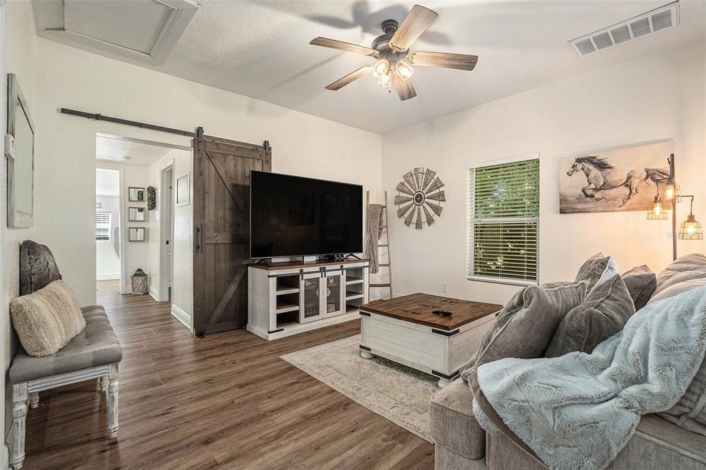 A living room features wood-look flooring, a sliding barn door, a ceiling fan, and furniture — 4921 6TH STREET, ZEPHYRHILLS, FL