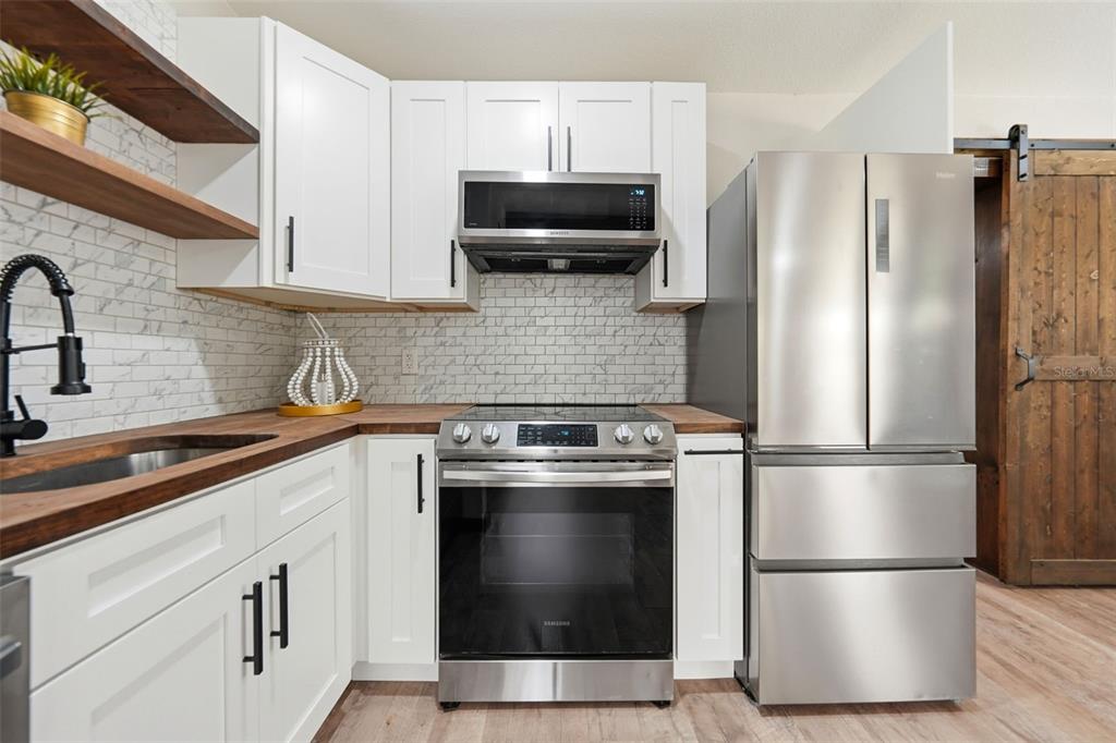 A kitchen features white cabinets, stainless steel appliances, wood countertops, and a marble tile backsplash — 906 SABRINA DRIVE, OCOEE, FL