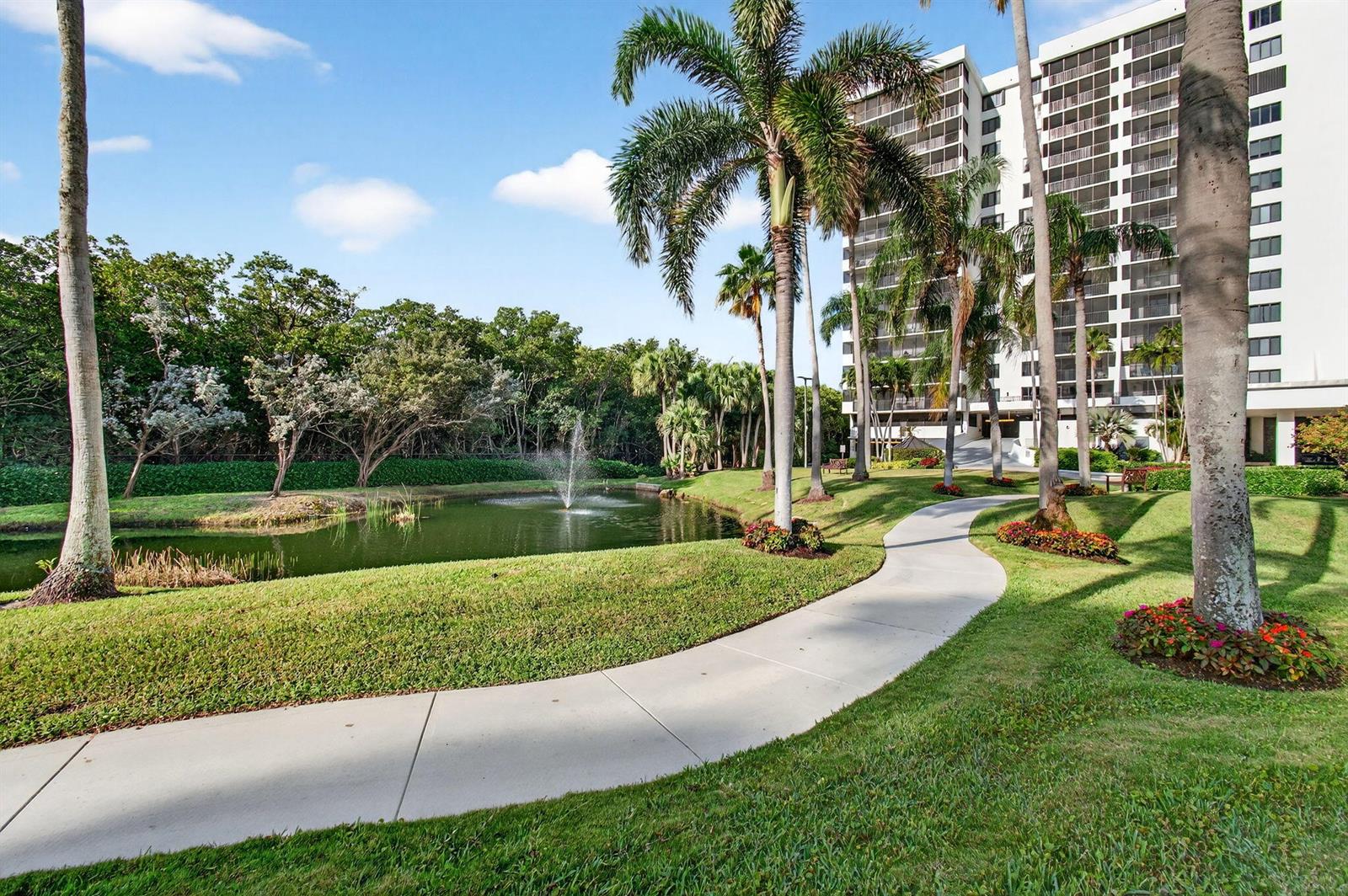 A paved walkway winds through a grassy lawn with palm trees and a small pond — 3420 S Ocean Boulevard # 5z, Highland Beach FL 33487, HIGHLAND BEACH, FL