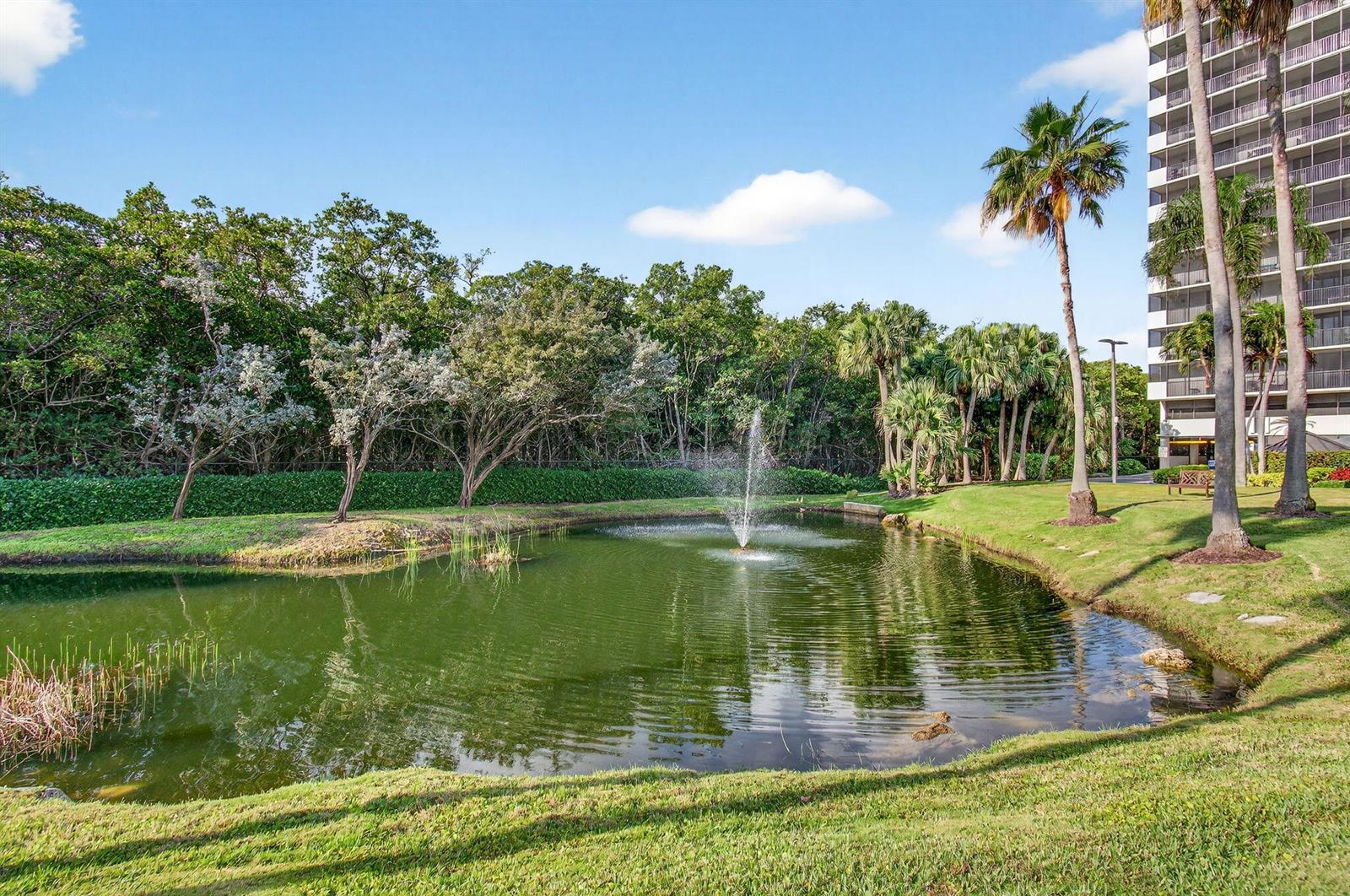 A pond with a fountain sits in front of a wooded area and a tall building — 3420 S Ocean Boulevard # 5z, Highland Beach FL 33487, HIGHLAND BEACH, FL