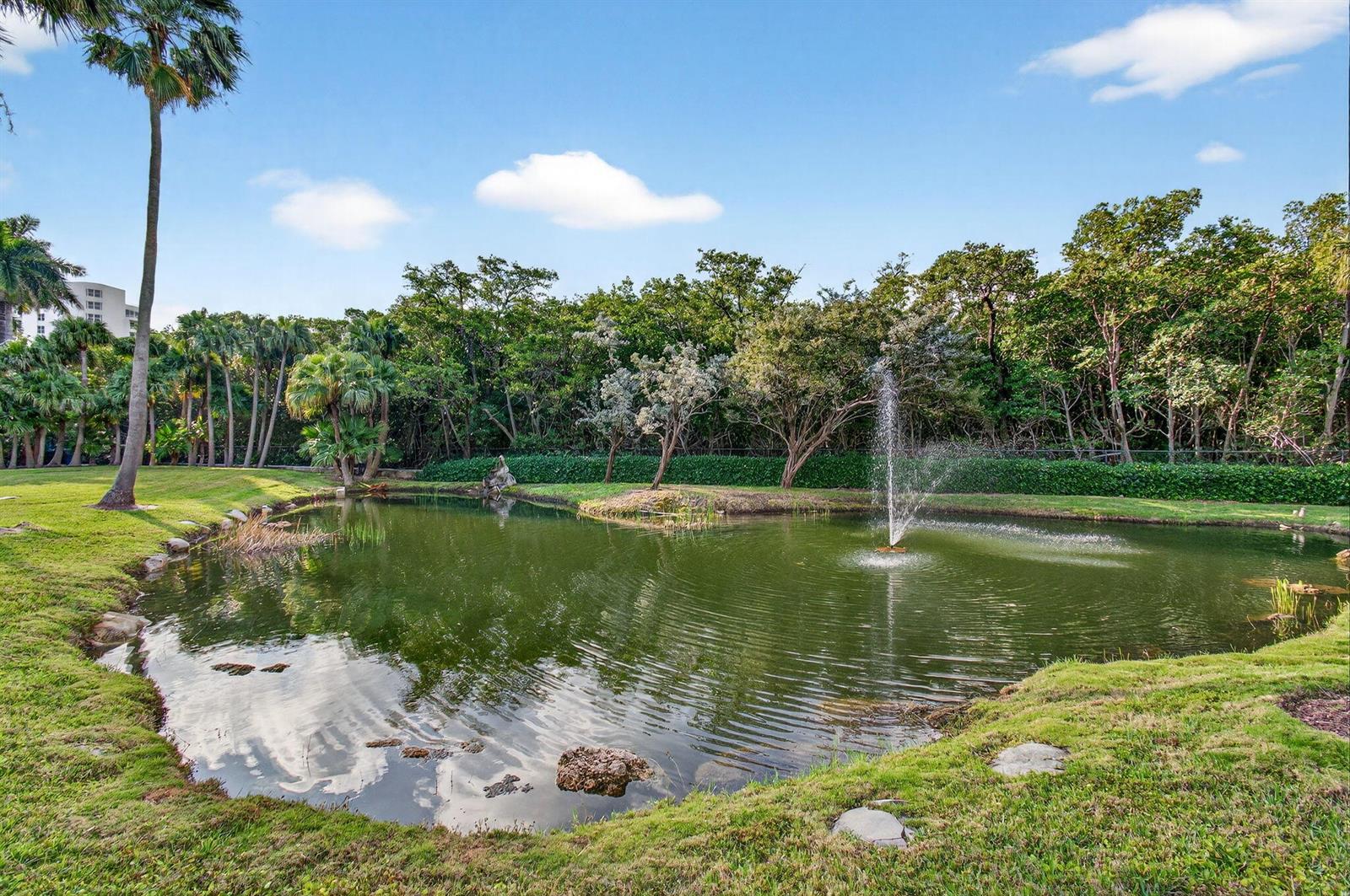 A small pond with a fountain is surrounded by a grassy lawn and dense trees — 3420 S Ocean Boulevard # 5z, Highland Beach FL 33487, HIGHLAND BEACH, FL