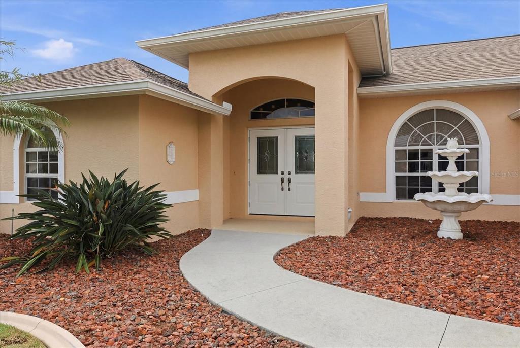 The exterior of a peach-colored house features a white double door and a stone fountain — 82 PINEHURST PLACE, ROTONDA WEST, FL