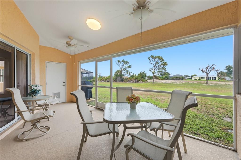 A screened-in patio with a dining set, ceiling fans, and a view of the yard — 82 PINEHURST PLACE, ROTONDA WEST, FL