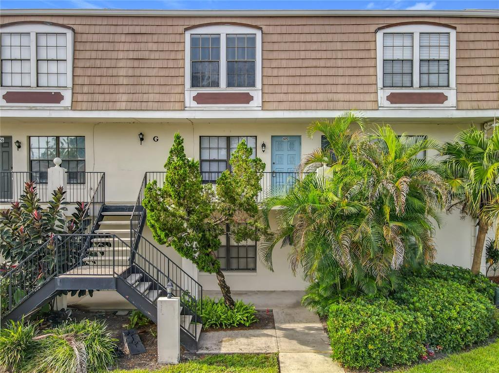 A two-story townhouse exterior features a blue front door, metal stairs, and palm trees — 6034 VILLAGE CIRCLE UNIT GE, ORLANDO, FL