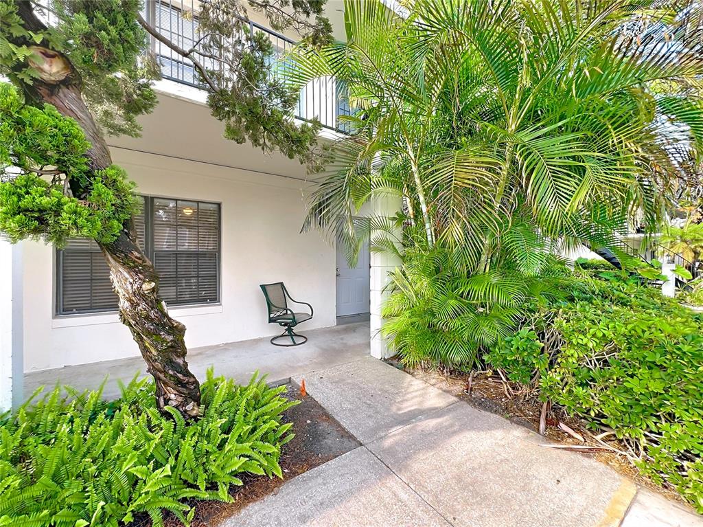 A ground-level patio features a single chair, a concrete walkway, and lush tropical landscaping — 6034 VILLAGE CIRCLE UNIT GE, ORLANDO, FL