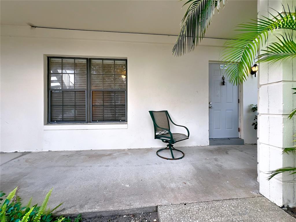 A concrete patio features a single green swivel chair, a window with blinds, and a door — 6034 VILLAGE CIRCLE UNIT GE, ORLANDO, FL