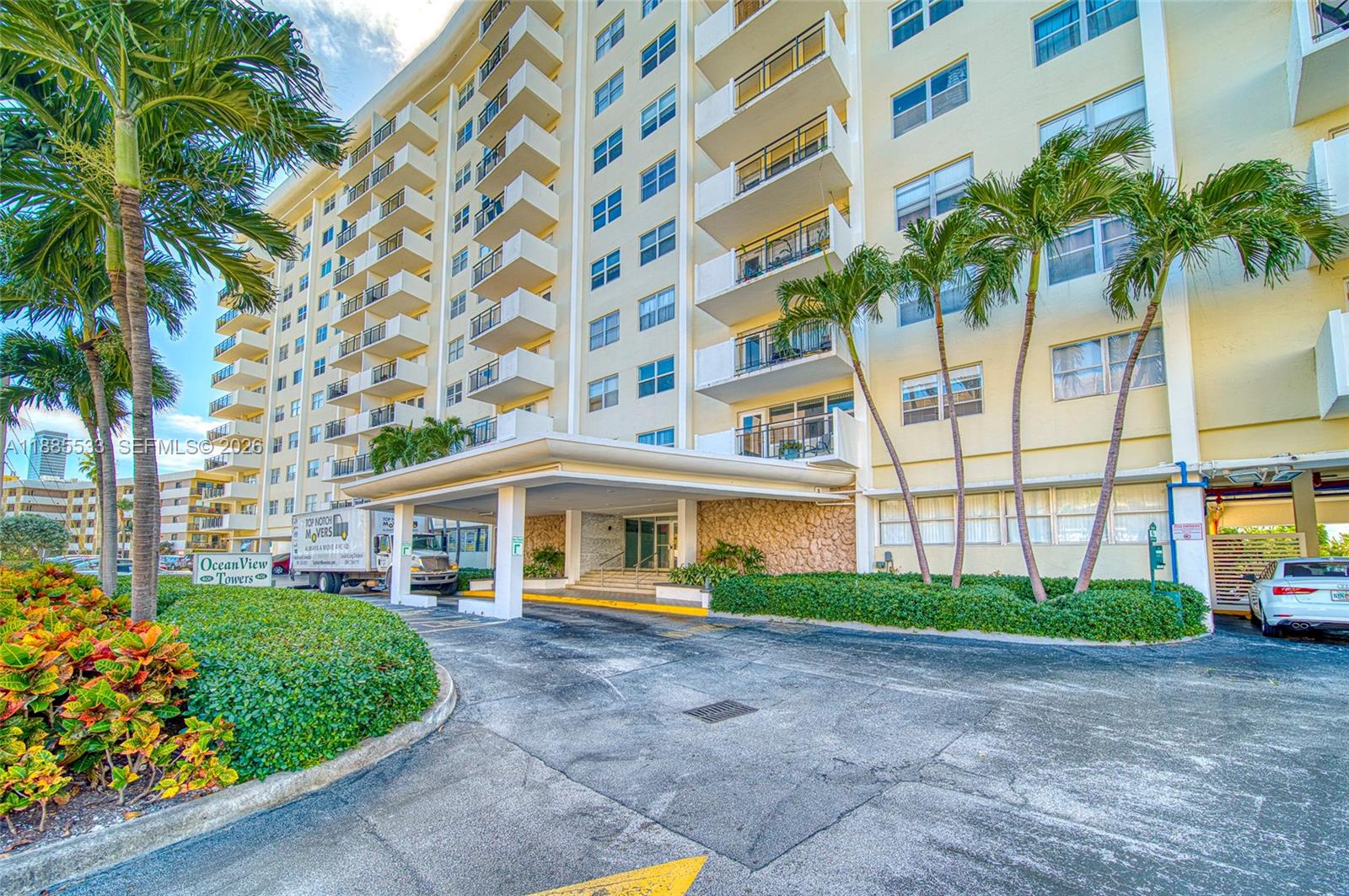 The exterior of a multi-story apartment building features a covered entrance and palm trees — 401 Golden Isles Dr # 908, Hallandale Beach FL 33009, HALLANDALE BEACH, FL