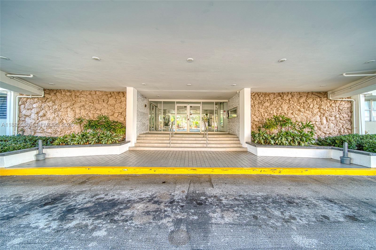 The building entrance features a covered driveway, stone walls, and glass doors with steps — 401 Golden Isles Dr # 908, Hallandale Beach FL 33009, HALLANDALE BEACH, FL