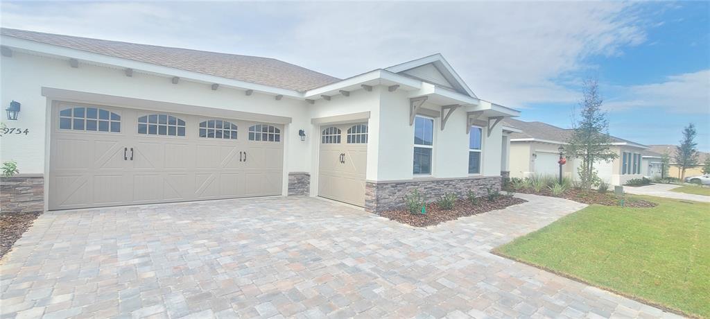 The exterior of a single-story house features a three-car garage, stone veneer, and paver driveway — 9754 SW 103RD AVENUE, OCALA, FL