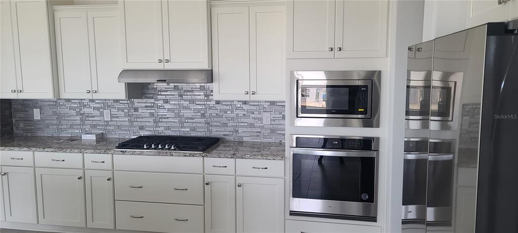 A kitchen features white cabinets, stainless steel appliances, a gas cooktop, and a tiled backsplash — 9754 SW 103RD AVENUE, OCALA, FL