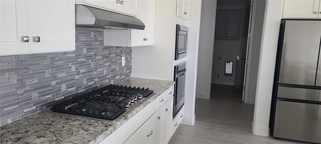 A kitchen features white cabinets, granite countertops, a gas cooktop, and a gray tile backsplash — 9754 SW 103RD AVENUE, OCALA, FL