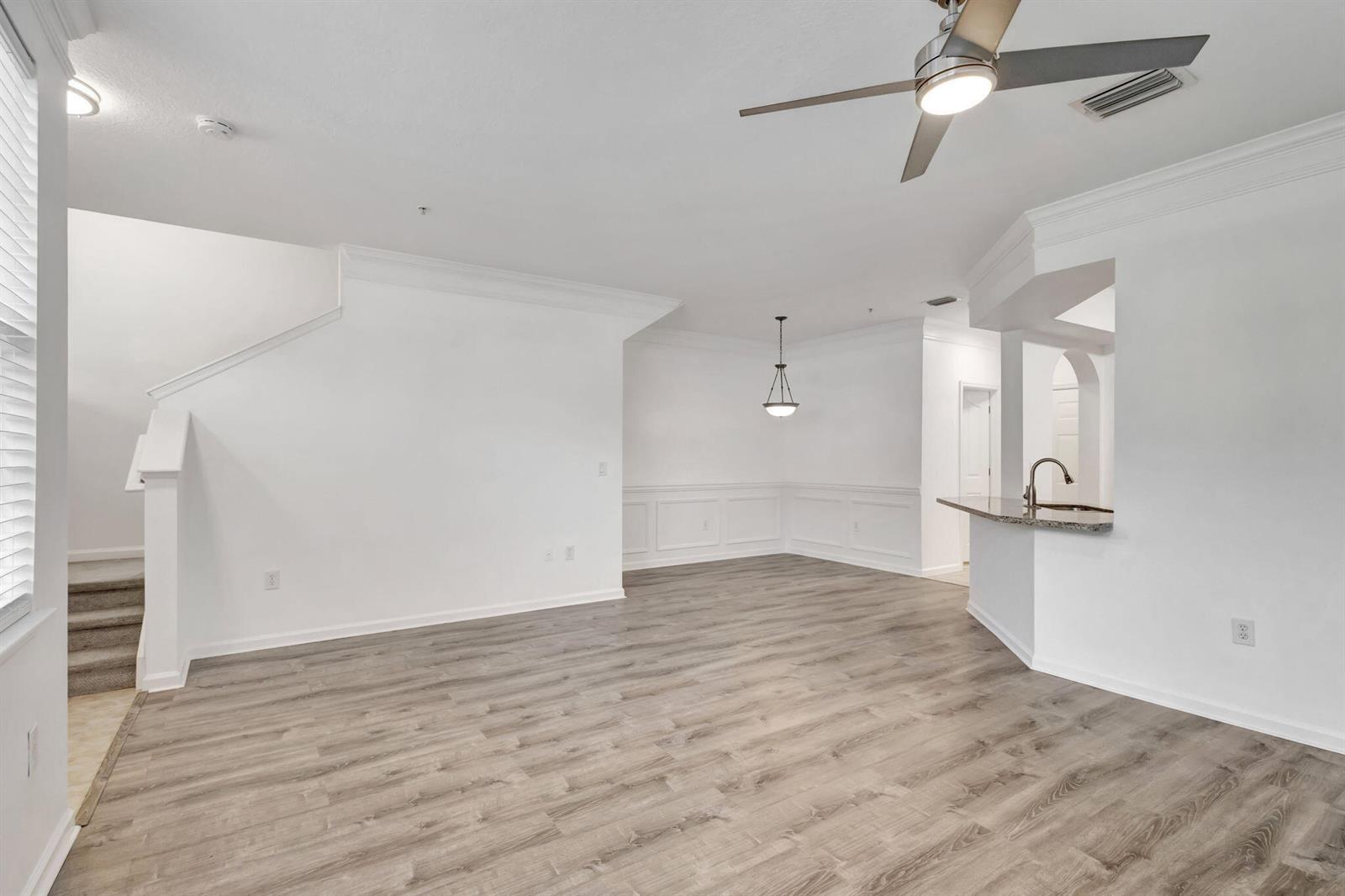 An open-concept living and dining area features white walls, wainscoting, and gray wood-look flooring — 826 Dakota Drive # 102, Jupiter FL 33458, JUPITER, FL