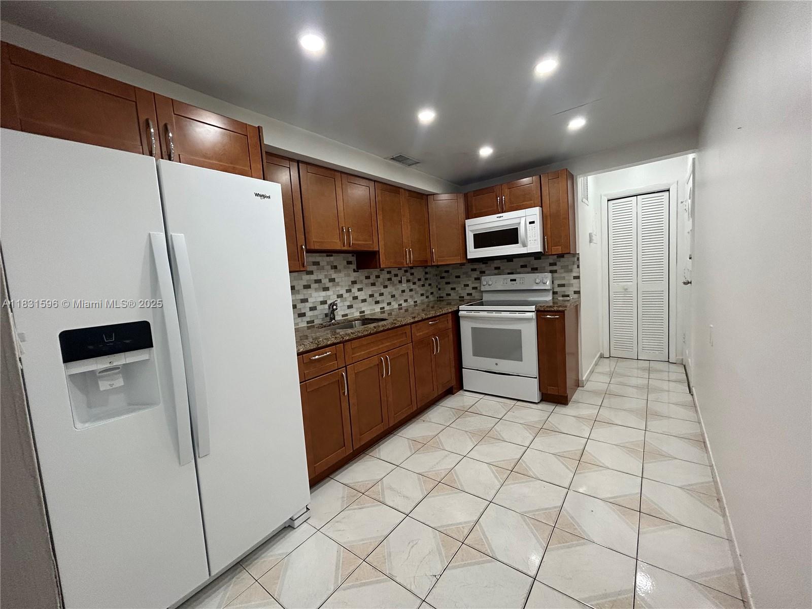 A kitchen features wood cabinets, granite countertops, white appliances, and light-colored tiled flooring — 1020 94th St # 202, Bay Harbor Islands FL 33154, BAY HARBOR ISLANDS, FL