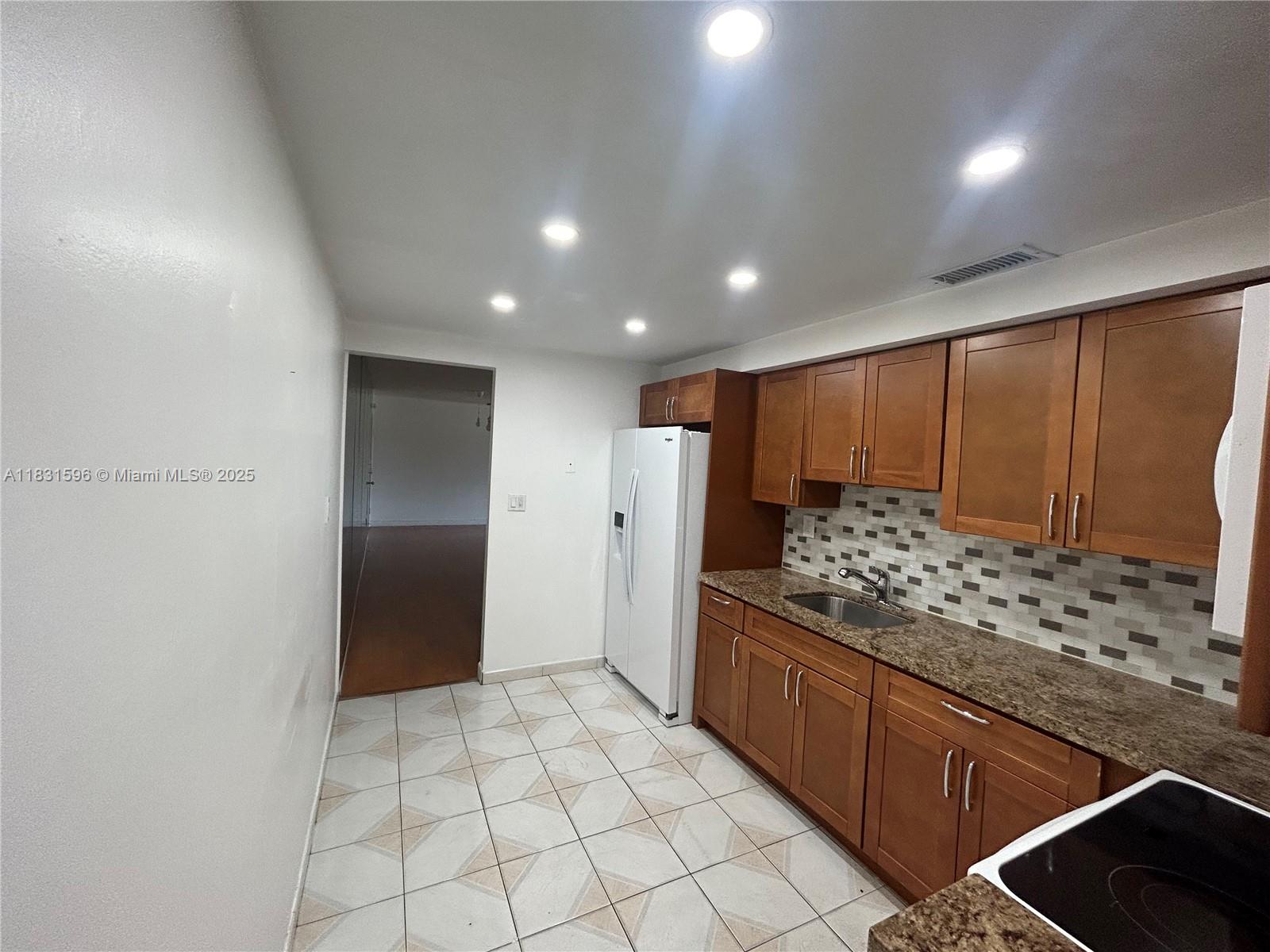 A kitchen features wood cabinets, granite countertops, a white refrigerator, and tiled flooring — 1020 94th St # 202, Bay Harbor Islands FL 33154, BAY HARBOR ISLANDS, FL