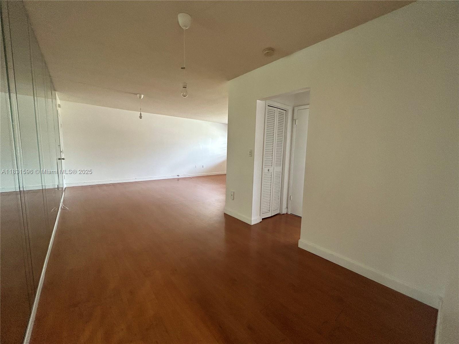 An empty room features wood-look flooring, white walls, and a mirrored closet wall — 1020 94th St # 202, Bay Harbor Islands FL 33154, BAY HARBOR ISLANDS, FL