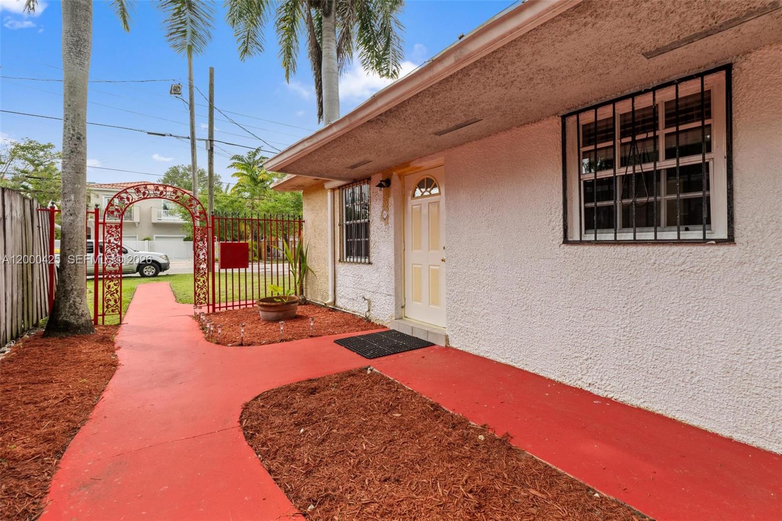 A white stucco house exterior features a red walkway, a metal gate, and barred windows — 3147 Mcdonald St # 2, Miami FL 33133, MIAMI, FL