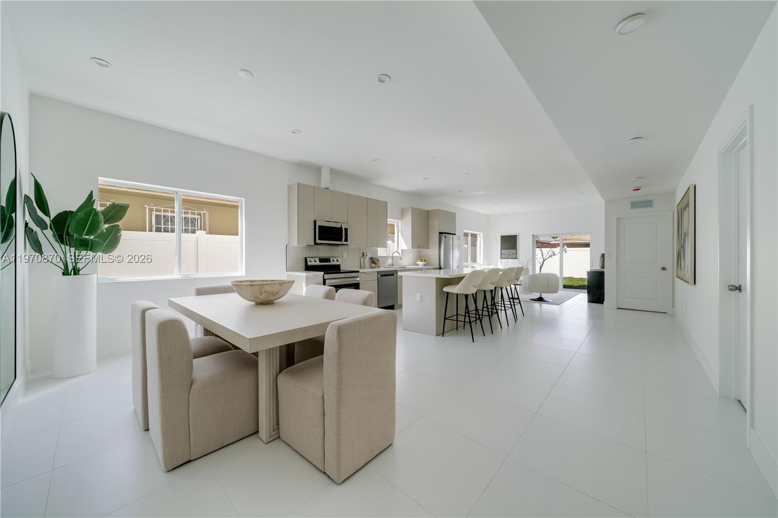 A modern open-concept kitchen and dining area features light-toned cabinetry, white tile floors, and seating — 5735 SW 4th St, Miami FL 33144, MIAMI, FL