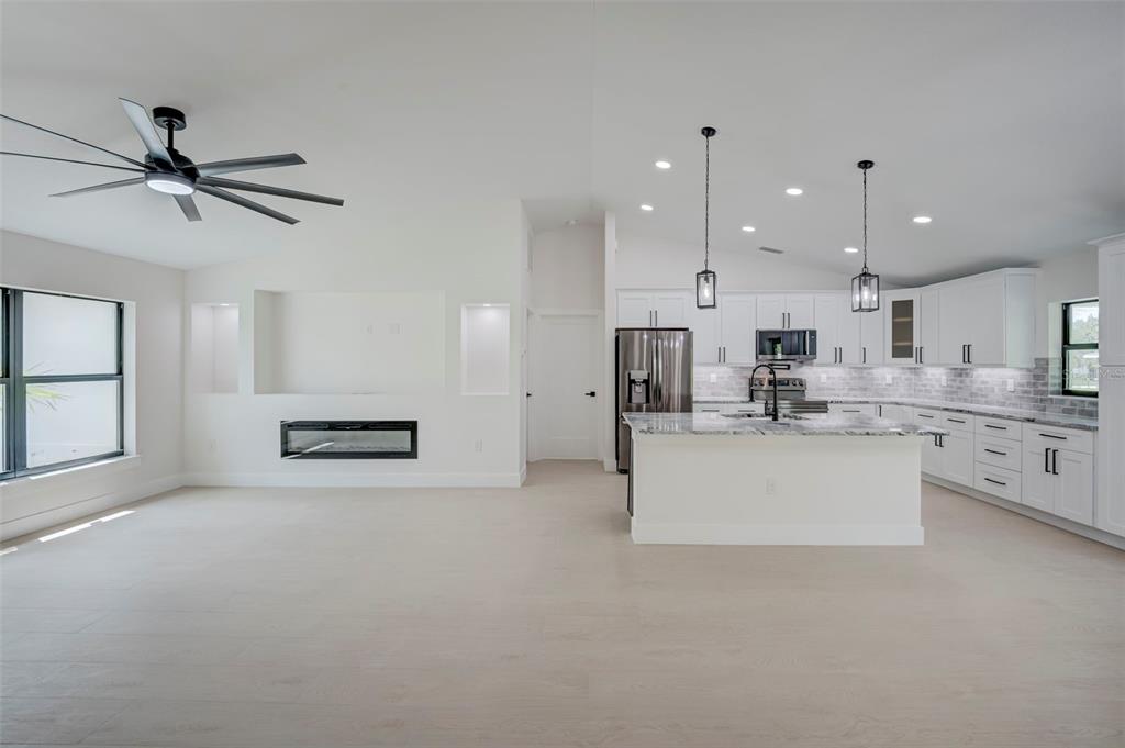 An open-concept kitchen and living area with white cabinets, a fireplace, and a ceiling fan — 7042 GROVE BOULEVARD, PUNTA GORDA, FL