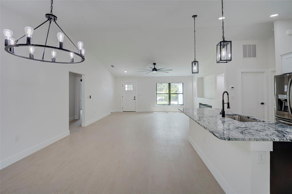 An open-concept kitchen and living area features light wood flooring, white walls, and pendant lighting — 7042 GROVE BOULEVARD, PUNTA GORDA, FL