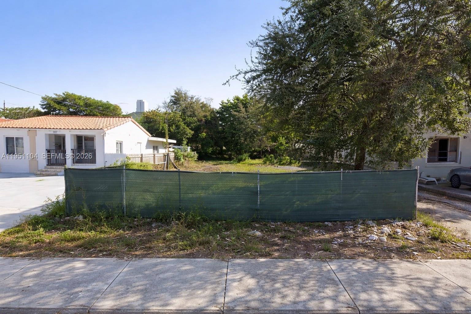 A vacant residential lot is enclosed by a green privacy fence between two houses — 161 NW 18th Ave, Miami FL 33125, MIAMI, FL