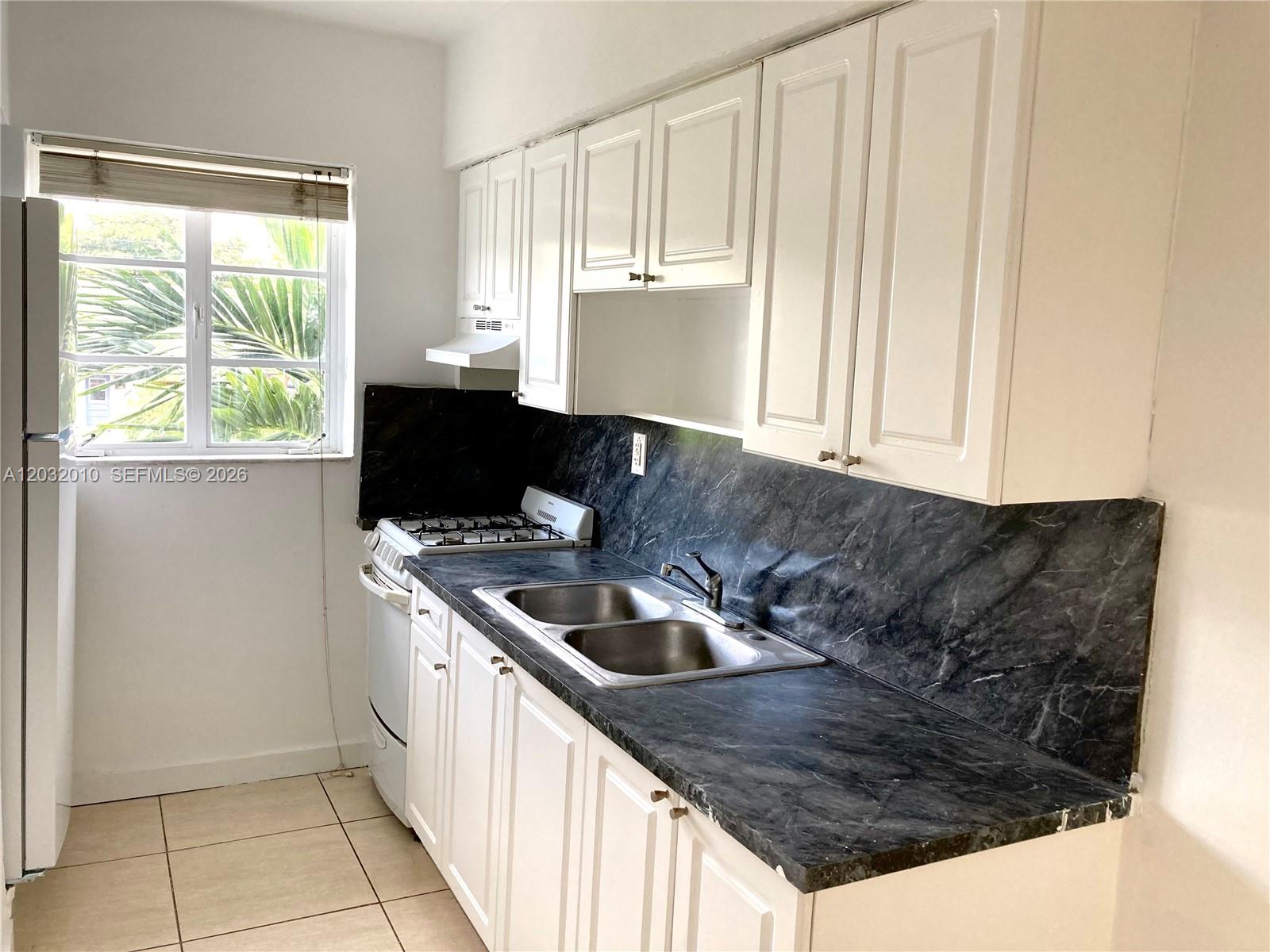 A kitchen features white cabinets, a dark marble-patterned countertop, and a stainless steel sink — 625 83rd St # 44, Miami Beach FL 33141, MIAMI BEACH, FL