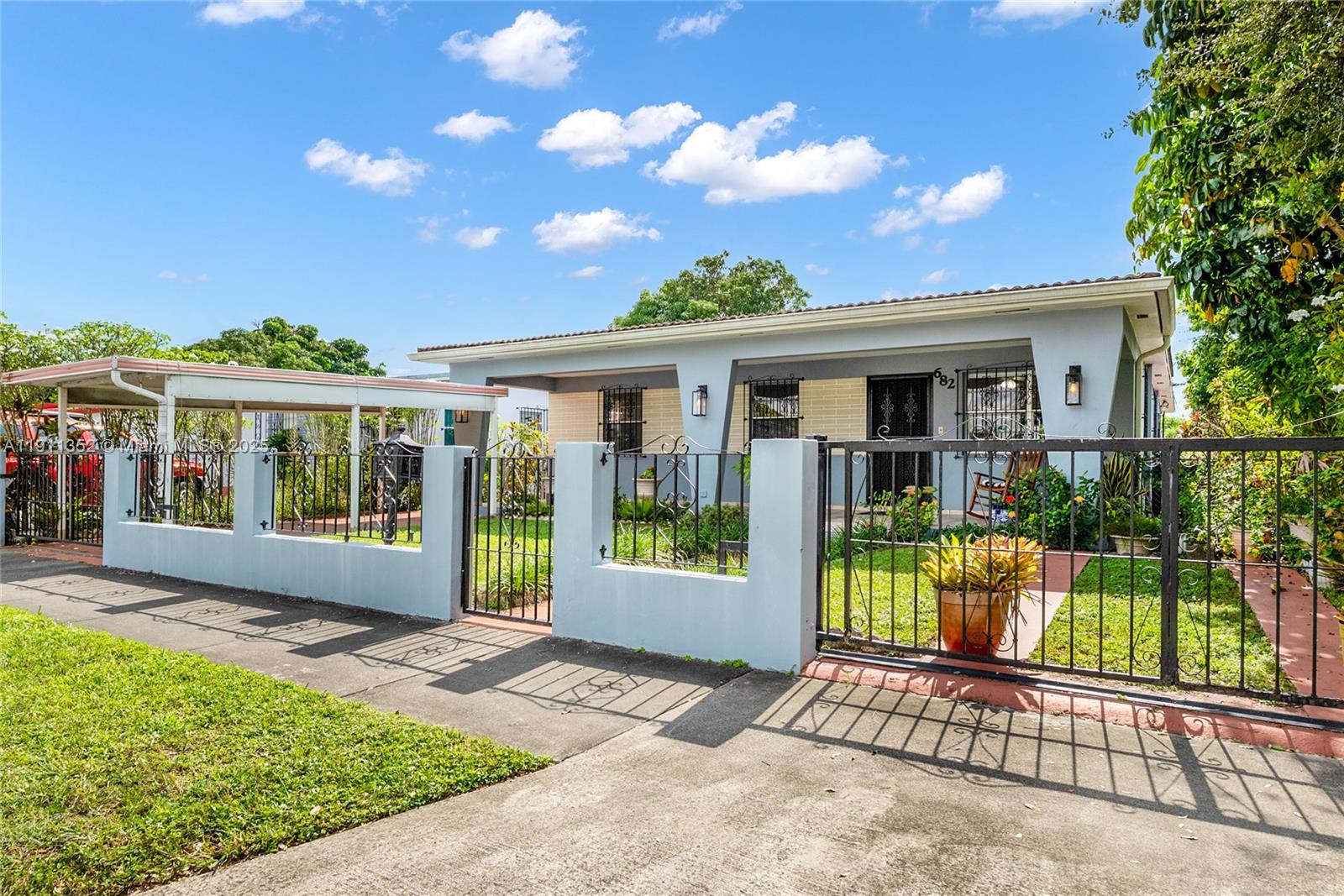 A light blue single-story house features a front porch, metal fencing, and a carport — 682 W 37th St, Hialeah FL 33012, HIALEAH, FL