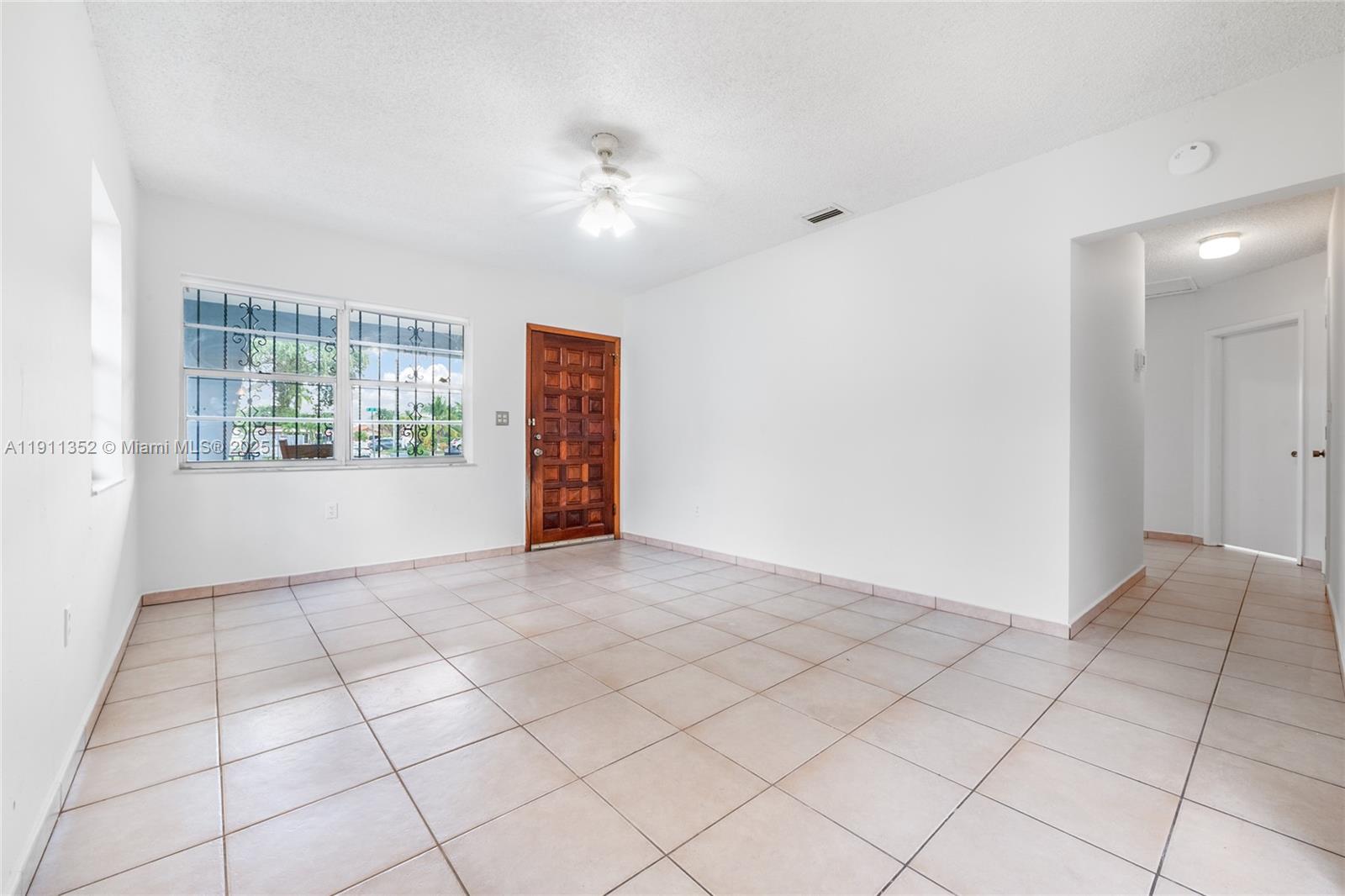 An empty room features white walls, light-colored floor tiles, a ceiling fan, and a wooden door — 682 W 37th St, Hialeah FL 33012, HIALEAH, FL