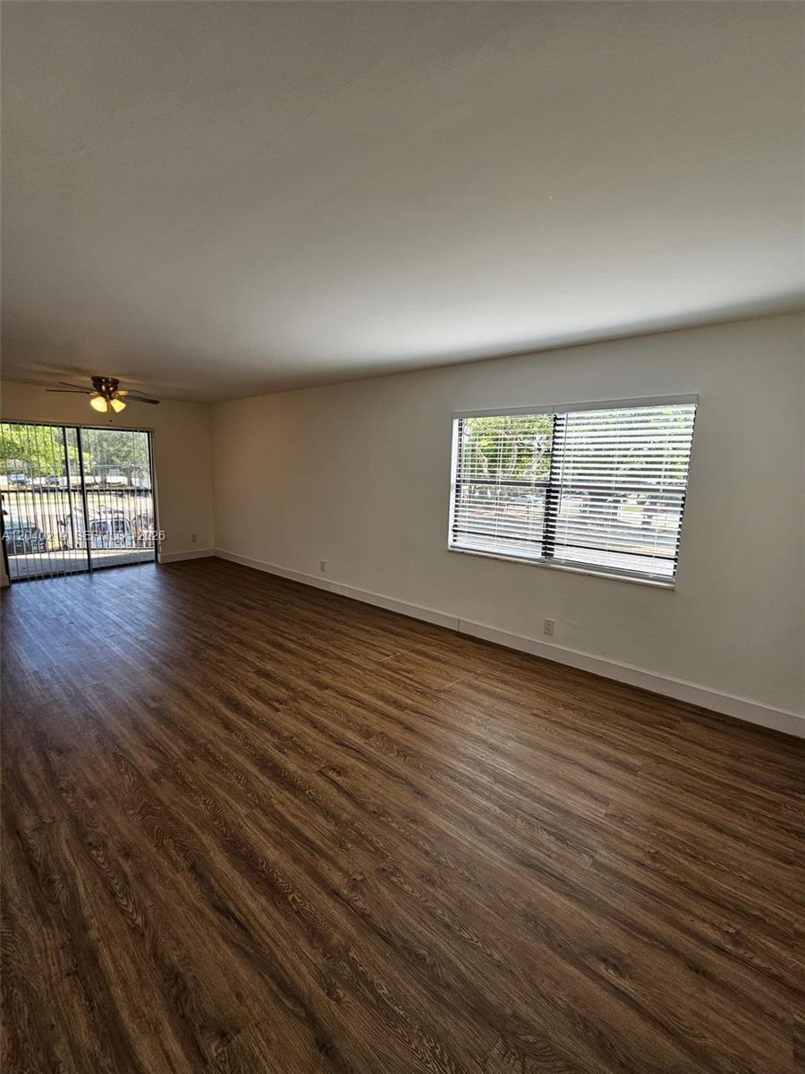 An empty living room features wood-look flooring, a ceiling fan, a sliding door, and a window — 3252 Foxcroft Rd # 216, Miramar FL 33025, MIRAMAR, FL