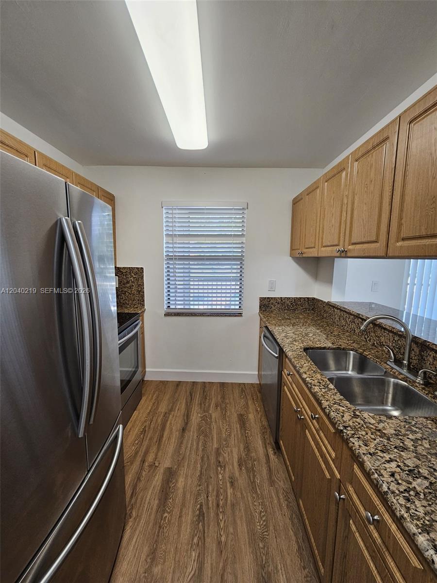 A galley kitchen features wood cabinets, granite countertops, stainless steel appliances, and wood-look flooring — 3252 Foxcroft Rd # 216, Miramar FL 33025, MIRAMAR, FL