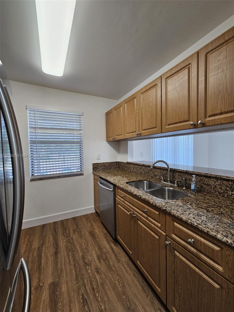 A kitchen features wood cabinets, granite countertops, a stainless steel dishwasher, and wood-look flooring — 3252 Foxcroft Rd # 216, Miramar FL 33025, MIRAMAR, FL