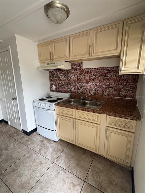 A kitchen features light-colored cabinets, a white stove, a double sink, and stone-patterned backsplash tiles — 14846 17TH STREET, DADE CITY, FL
